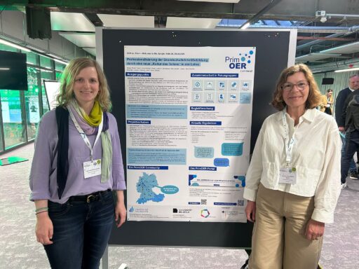 Auf dem Bild sind Bernadette Bernasconi (links) und Anna-Maria Kamin (rechts) zu sehen. In der Mitte ist das PrimOER-Poster auf einer Pinnwand zu sehen.